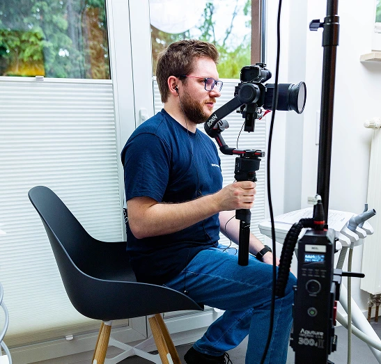 Simon Rüger sitzt als Videograf auf einem Stuhl während einer Videoproduktion und hält seine Kamera in der Hand, während er konzentriert schaut