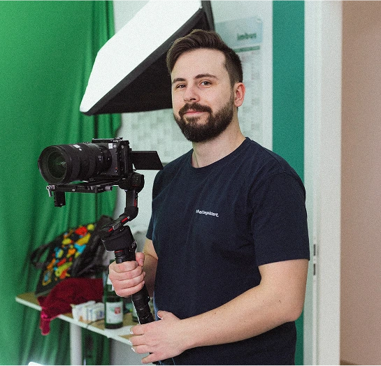 Ein Videograf von wirdenkenlokal steht mit seiner Kamera in einem Büro während einer Produktion und lächelt in die Kamera