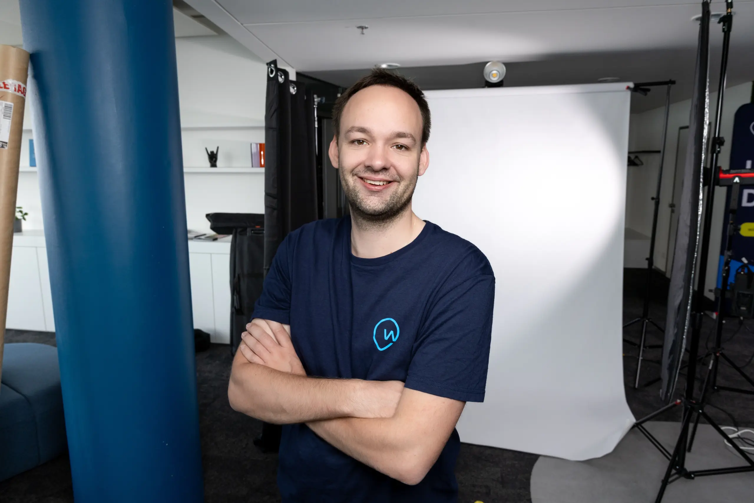 Constantin Kaindl lächelt in die Kamera mit verschränkten Armen vor der Kulisse eines Videosets