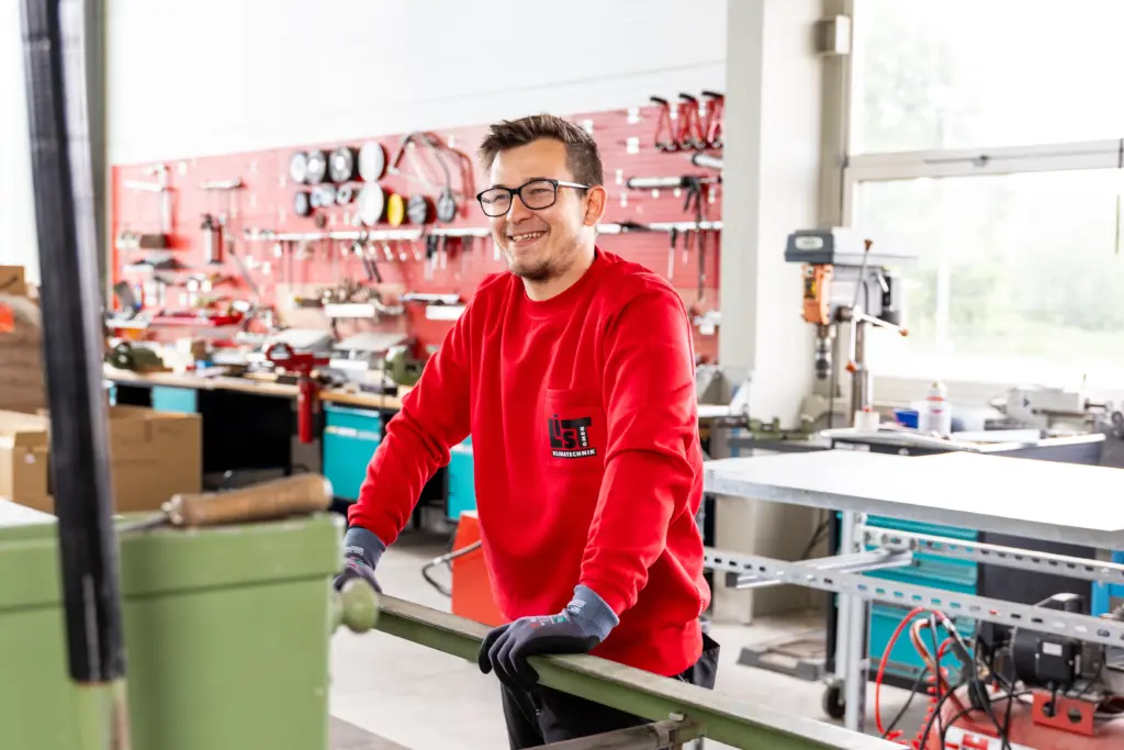 Ein Mitarbeiter der List GmbH steht in Arbeitskleidung lächelnd in ihrer Werkstatt.